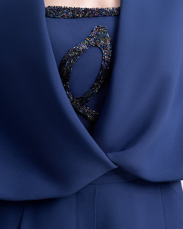 Close-up of a navy draped bolero revealing part of a strapless beaded top underneath, featuring intricate multicolored beadwork on crepe fabric.
