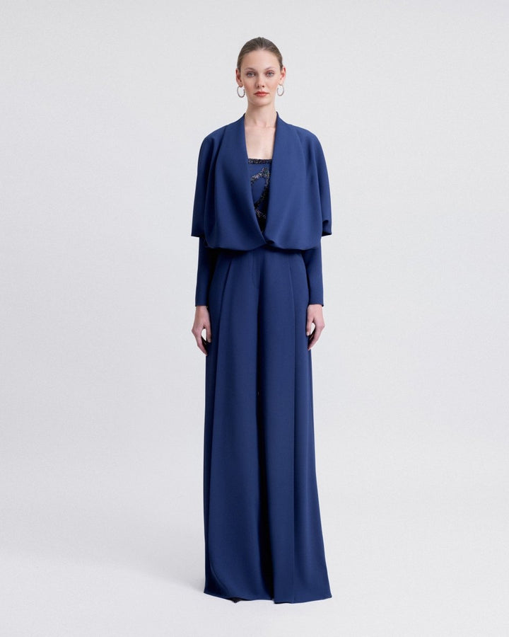A navy ensemble featuring a strapless beaded top with high-waisted straight-cut pants, styled with a matching draped bolero with a plunging neckline and long sleeves.