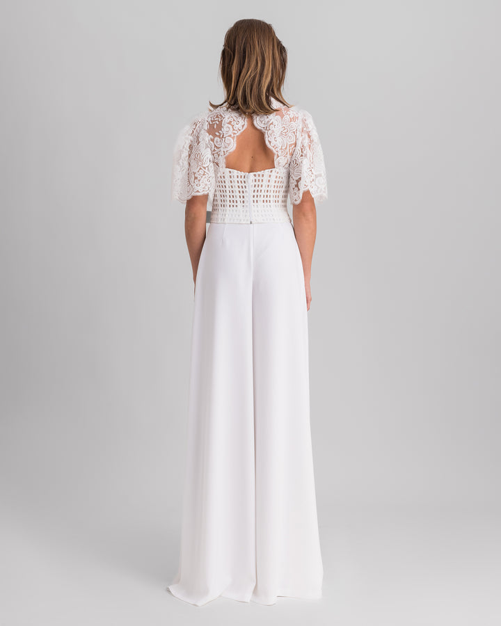 The back of a white evening wear set featuring a lace top with flared sleeves and an open back,  paired with flared crepe pants.
