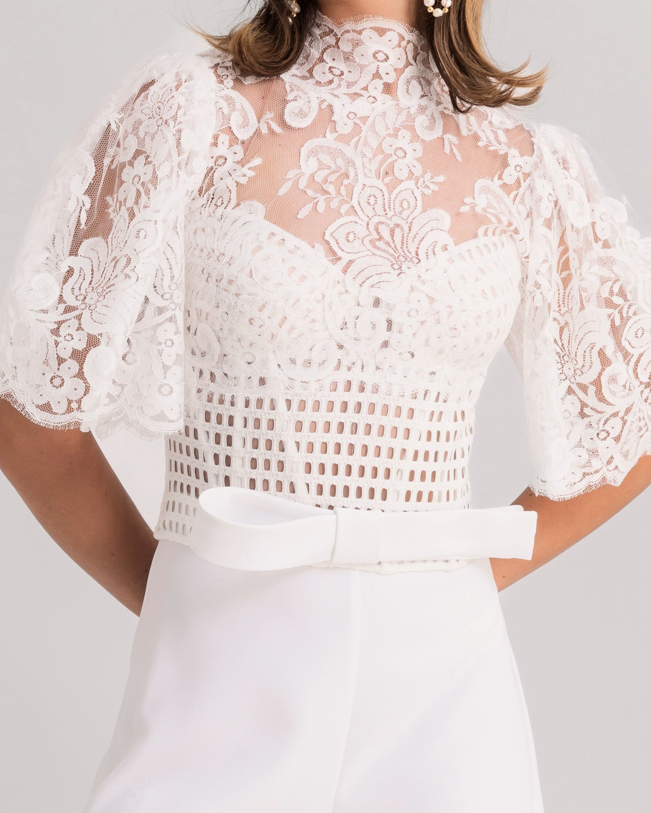 A close-up of a white evening wear set featuring a high-collar lace top with flared sleeves paired with flared crepe pants.
