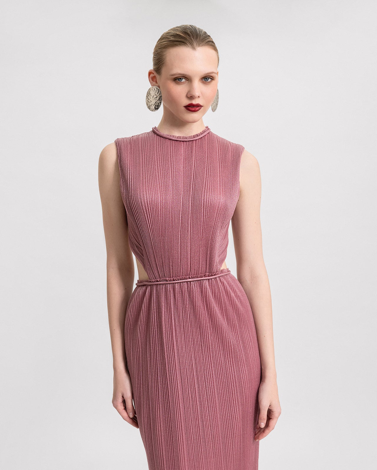 Video of a long, slim-cut pink shimmer dress with pleated fabric, waist cut-outs, and an open back, shown from multiple angles to highlight the fit and movement.
