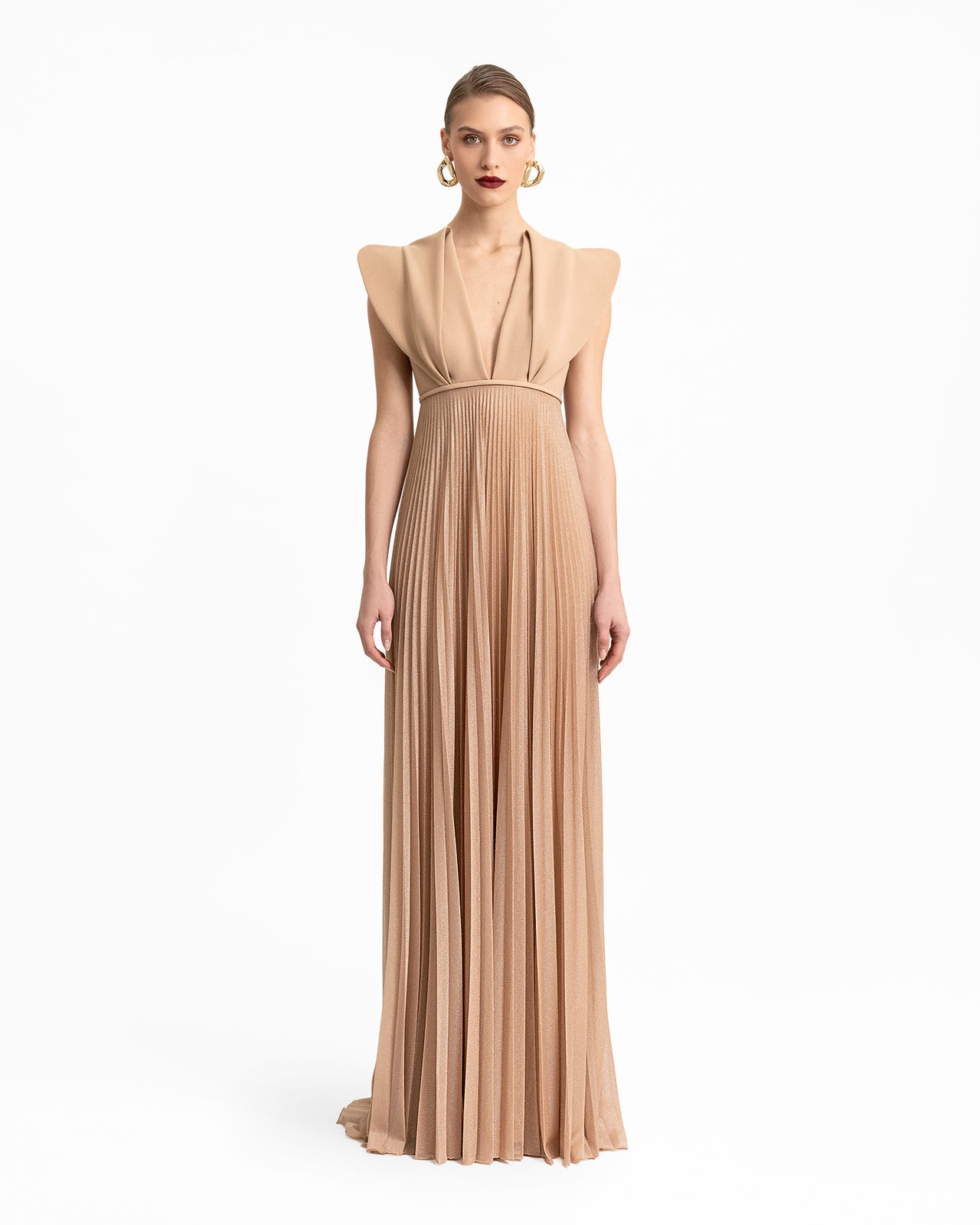 Video of a long beige dress with structured shoulders, a deep V-neckline, and a pleated shimmer skirt, showcasing the design’s movement and elegant silhouette from different angles.