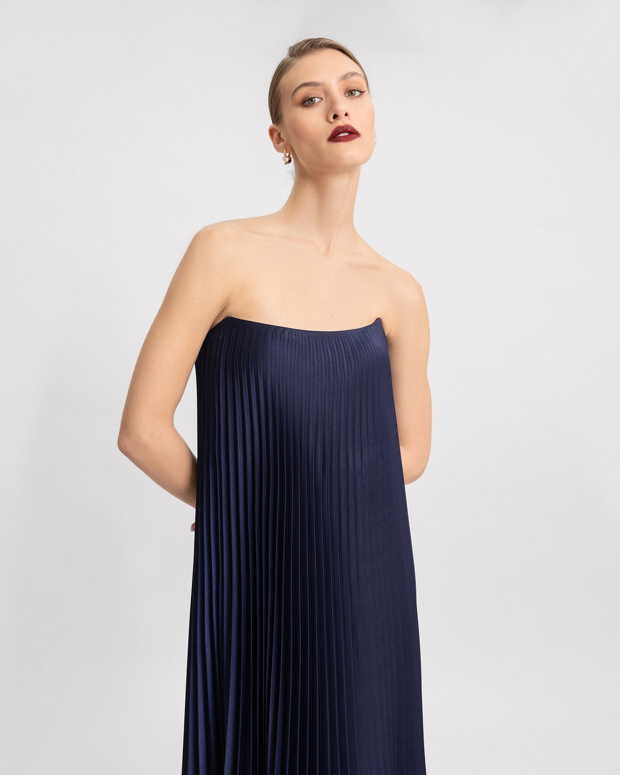 Video of a strapless navy blue pleated gown. The camera captures the fluid motion of the vertical pleats as the model moves, emphasizing the dress’s graceful, flowy silhouette and elegant simplicity.