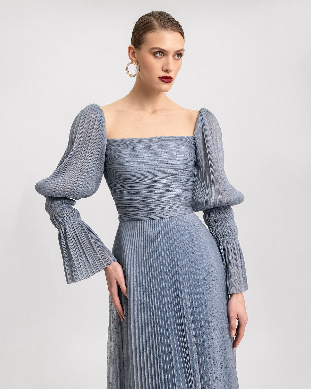Video of a dusty blue shimmer dress with a square neckline, puffed long sleeves, ruched bodice, and a pleated flowy skirt, shown from multiple angles in motion.