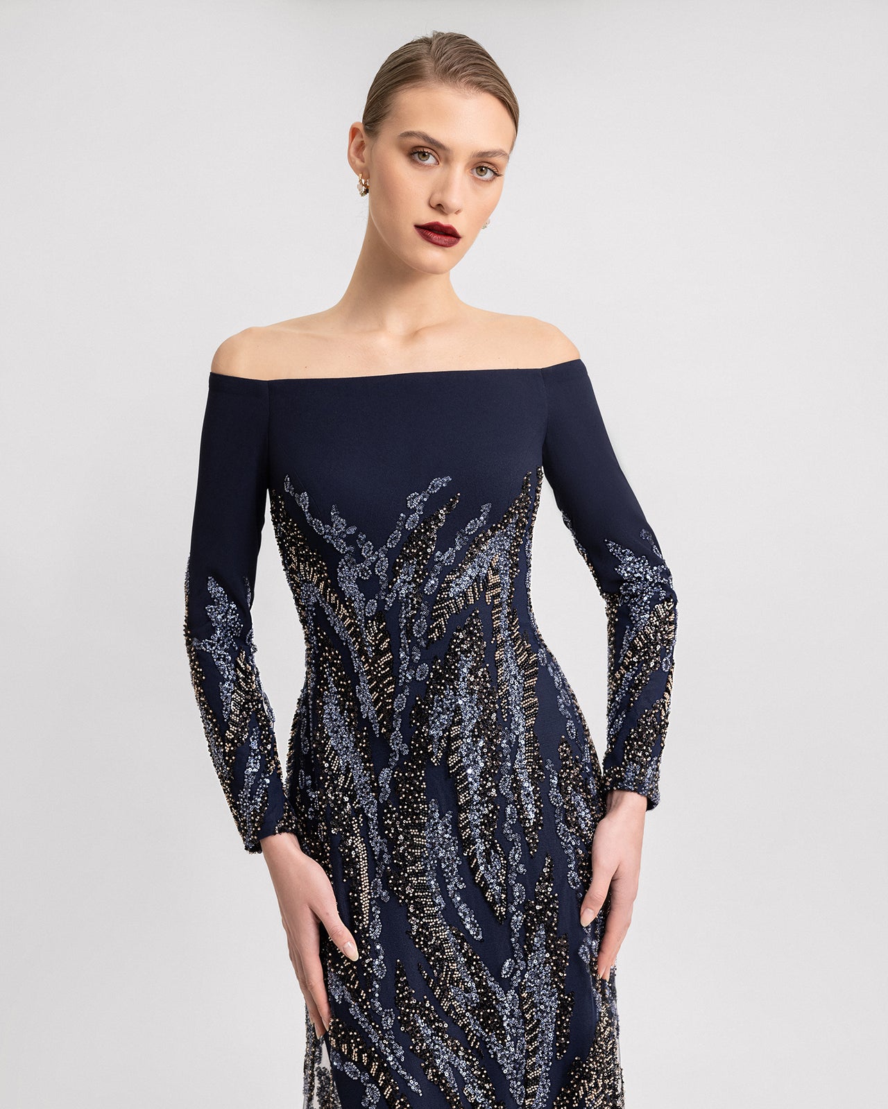 Video of an off-the-shoulder navy gown with long sleeves, featuring detailed blue and gold beadwork over crepe and tulle fabric. The floor-length dress moves gracefully, showcasing its intricate embroidery.