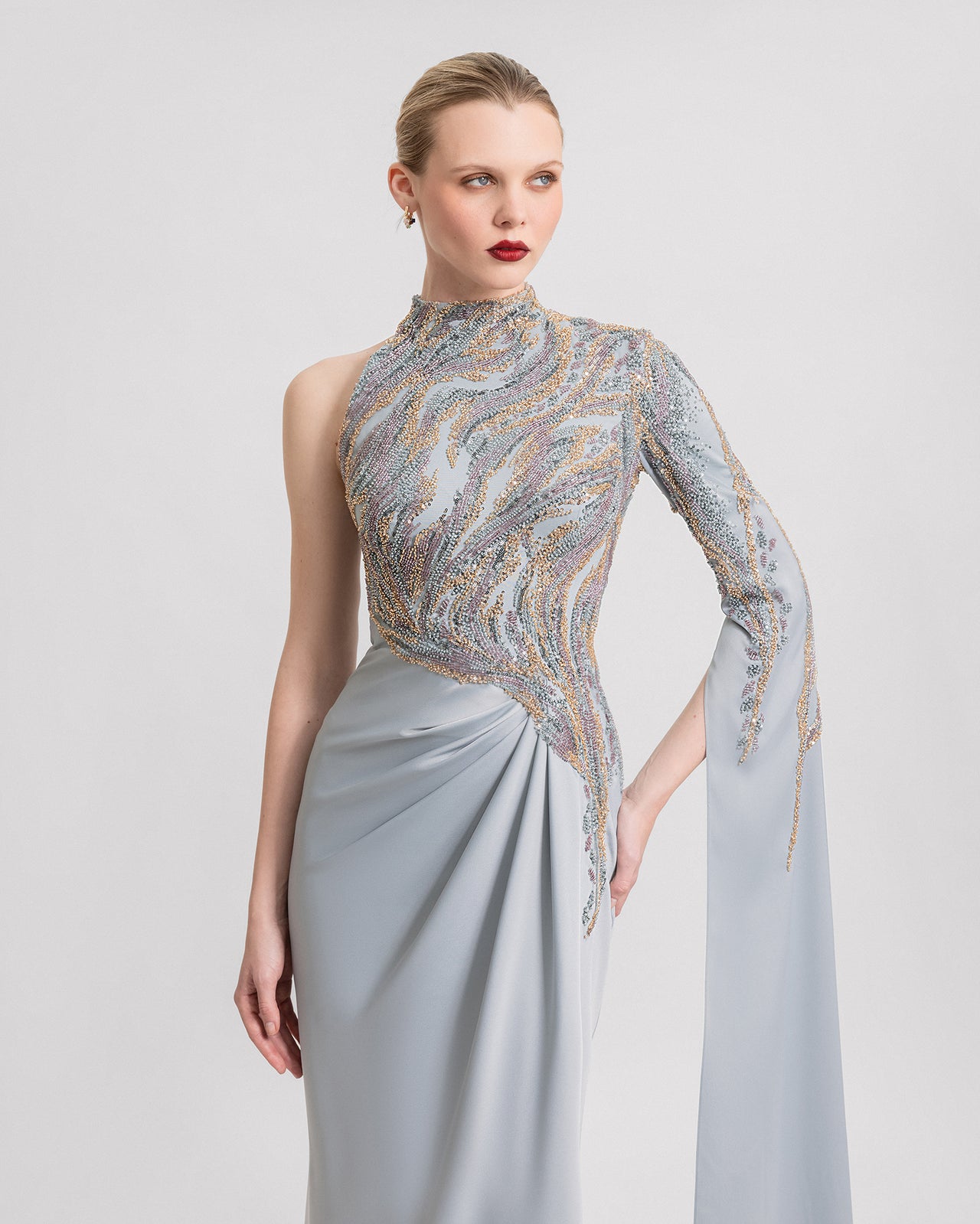 Video of an asymmetrical light blue dress with beaded tulle bodice, one floor-length sleeve, and a draped satin skirt with a side slit, shown from multiple angles in motion.
