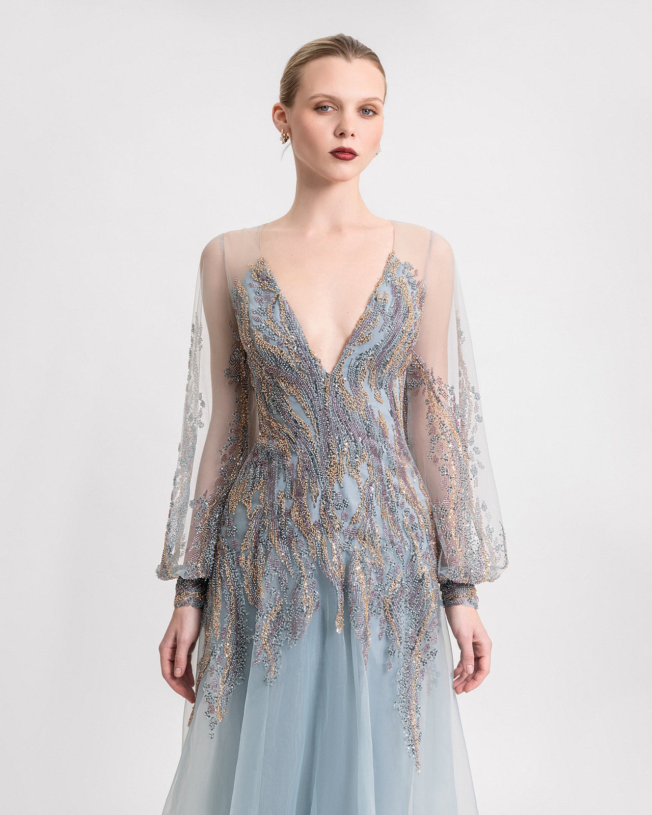Video of a teal blue gown with a plunged V-neckline, beaded sheer sleeves, and a flowy organza skirt, shown from multiple angles to highlight its movement and detailing.