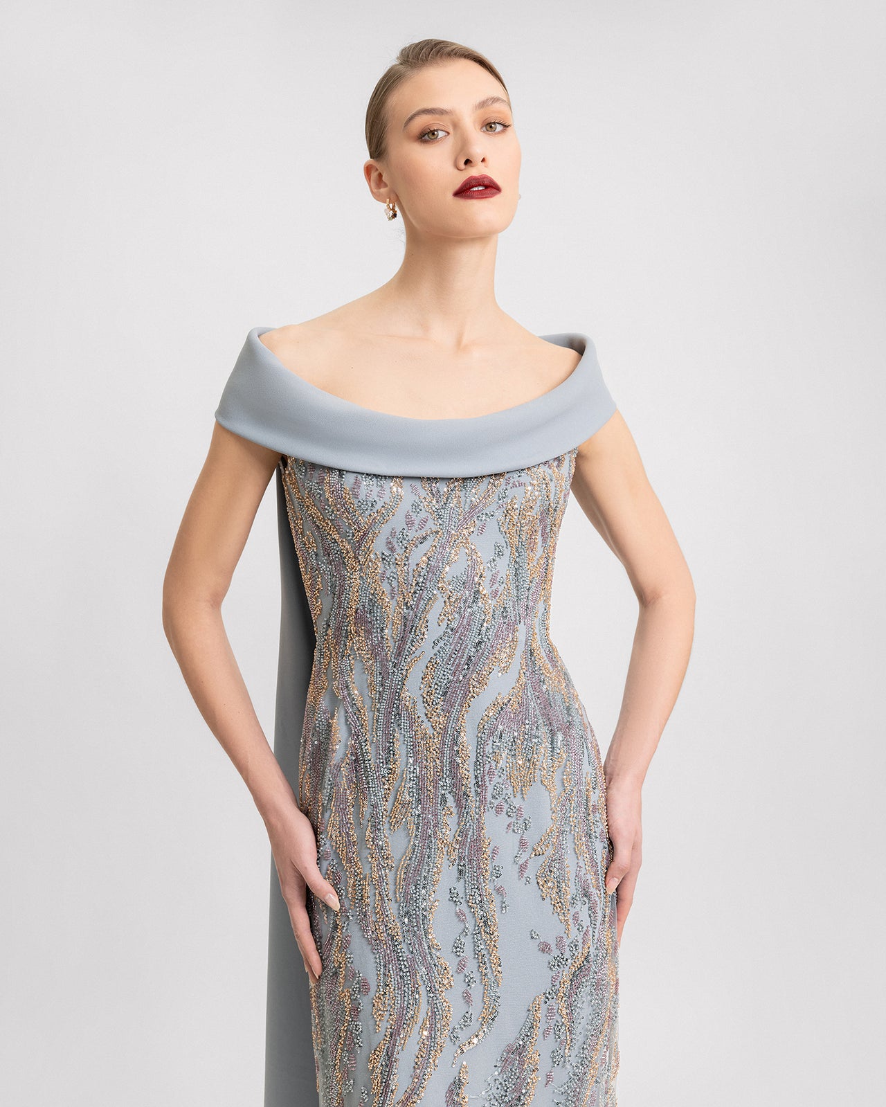 Video of an off-the-shoulder light blue slim-cut dress with intricate beaded embroidery and a long flowing cape, shown from multiple angles in motion.
