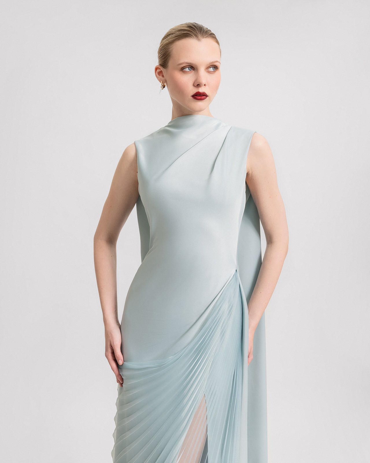 Video of an aqua blue slim-cut satin dress with a high neckline, pleated sheer organza overskirt, side slit, and flowing cape, shown from various angles in motion.