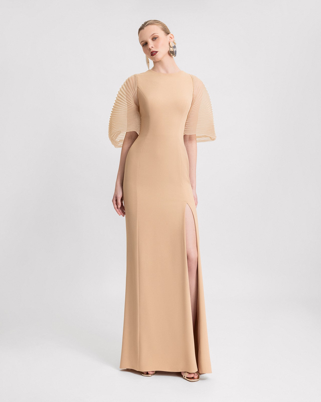 Video of a woman modeling a long beige dress with pleated organza sleeves, a side slit, and a large bow detail at the back, showcasing the dress from different angles as she moves.