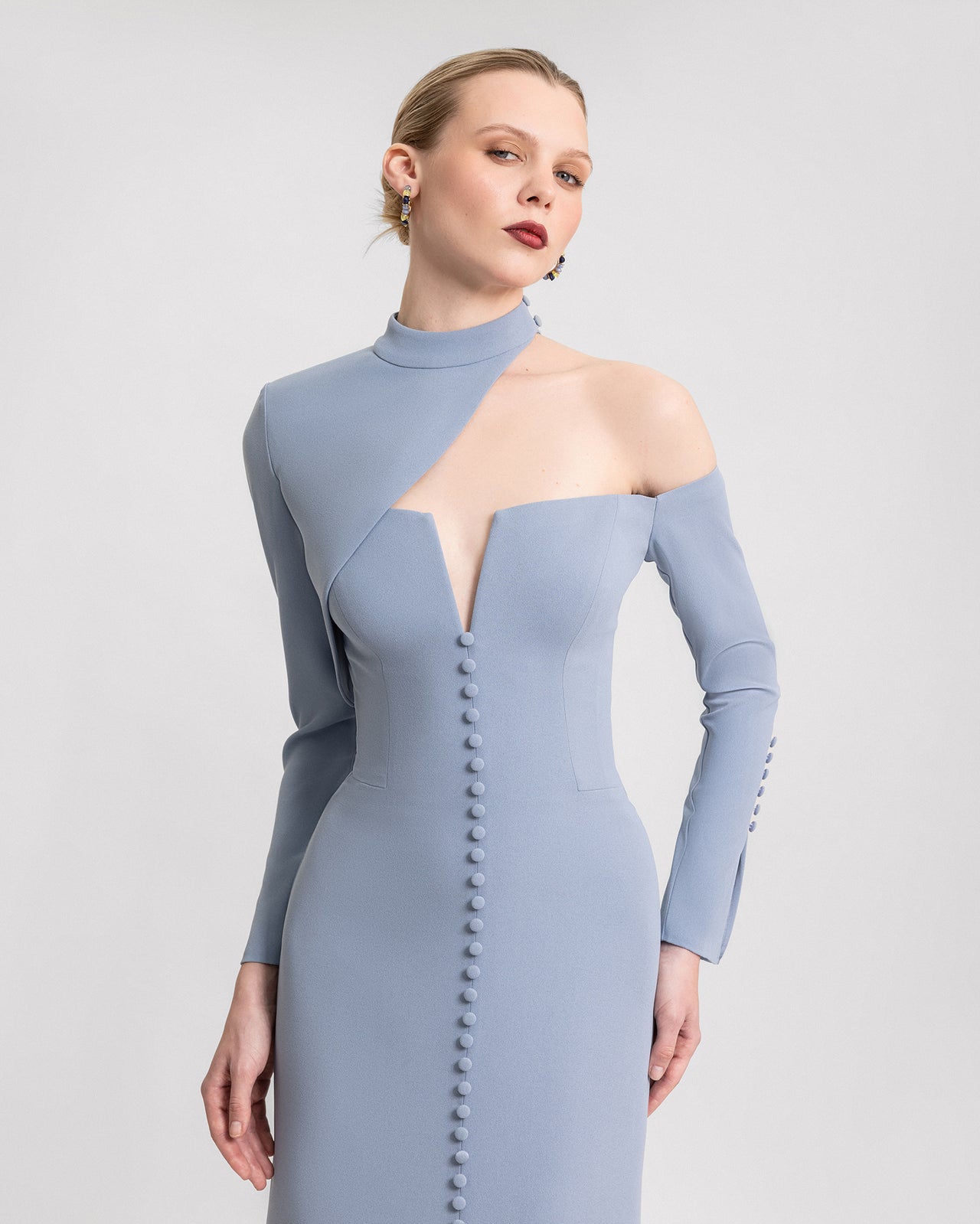 Video of a dusty blue off-the-shoulder dress with an asymmetrical button-down top, front slit, and long sleeves, shown from multiple angles to highlight the unique neckline and elegant silhouette.