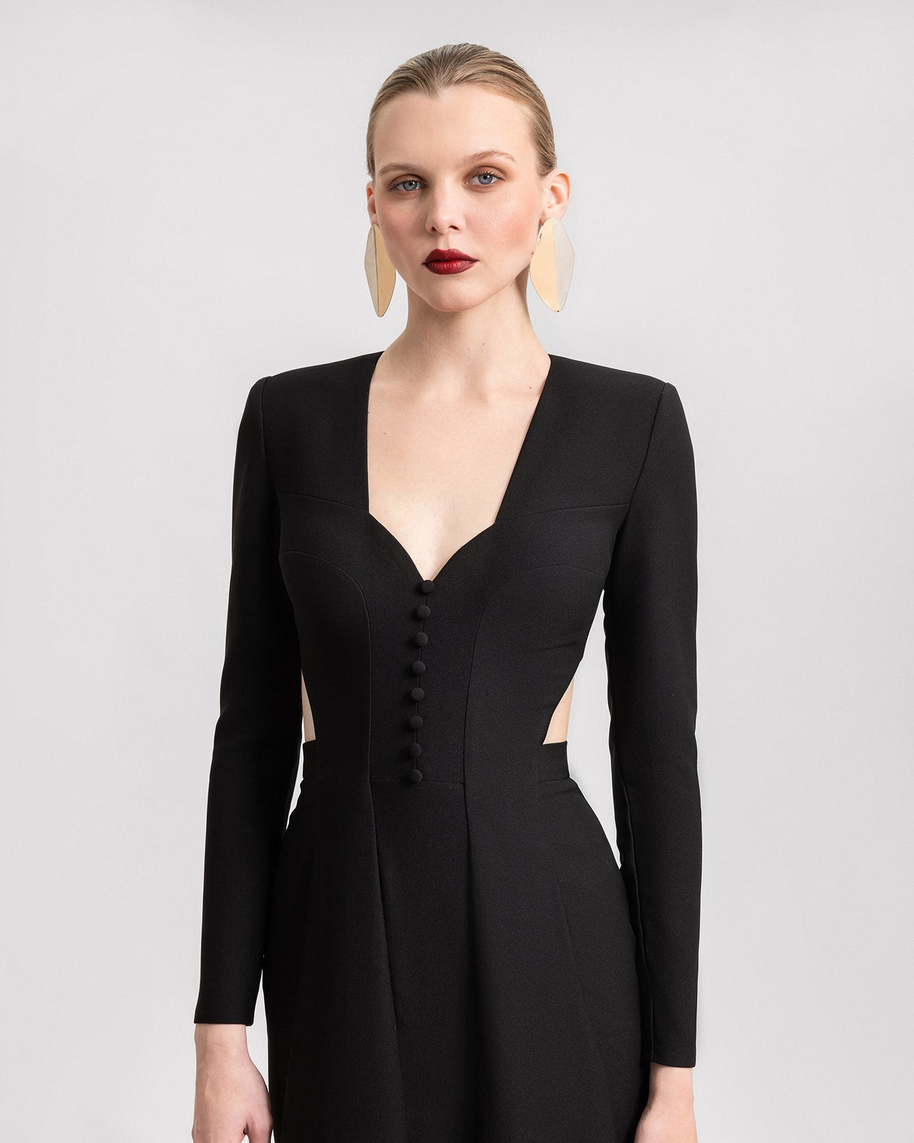 Video of a black crepe gown with long sleeves, a deep buttoned-down neckline, side waist cut-outs, and an open back. The footage highlights the dress’s sleek silhouette and bold design as the model walks and turns.
