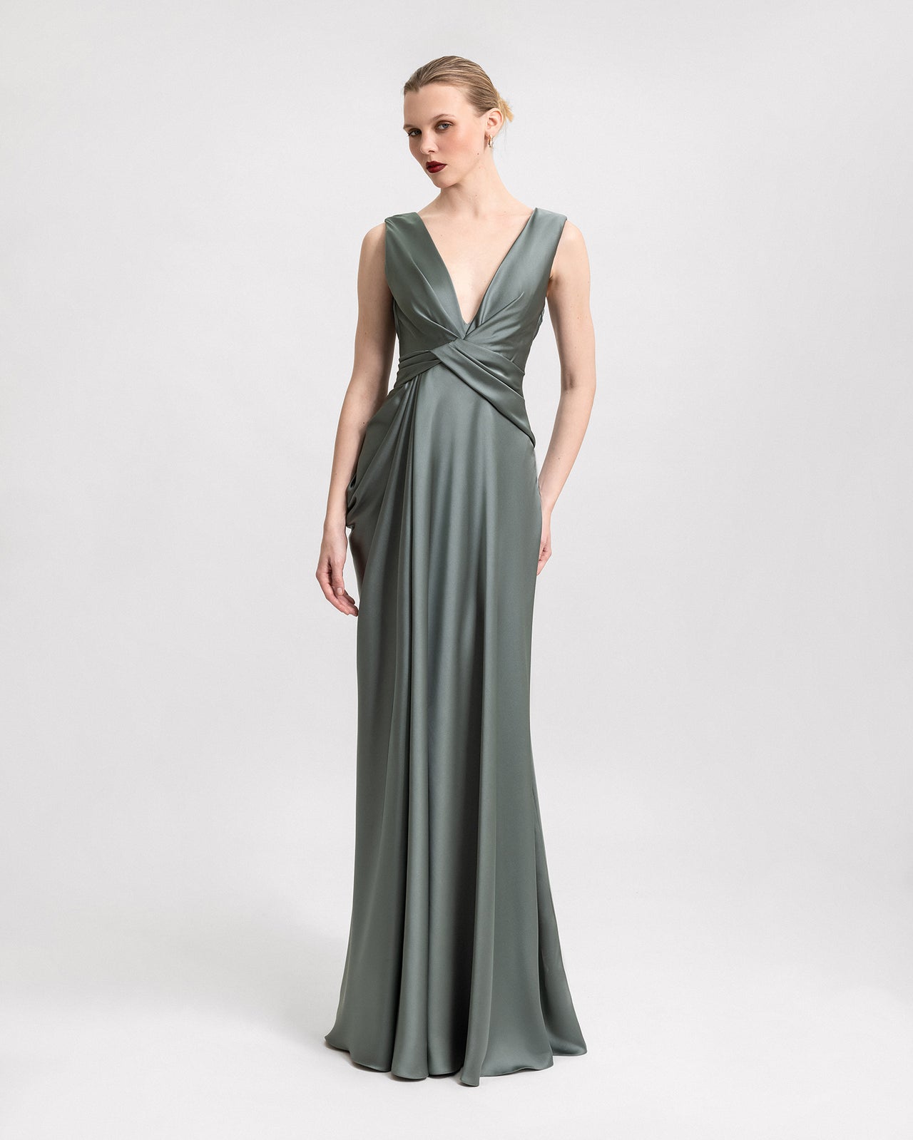 Video of a long satin sage green dress with a plunging V-neckline, asymmetrical draped waist, and deep V-back, highlighting the elegant fit and fluid movement from multiple angles.