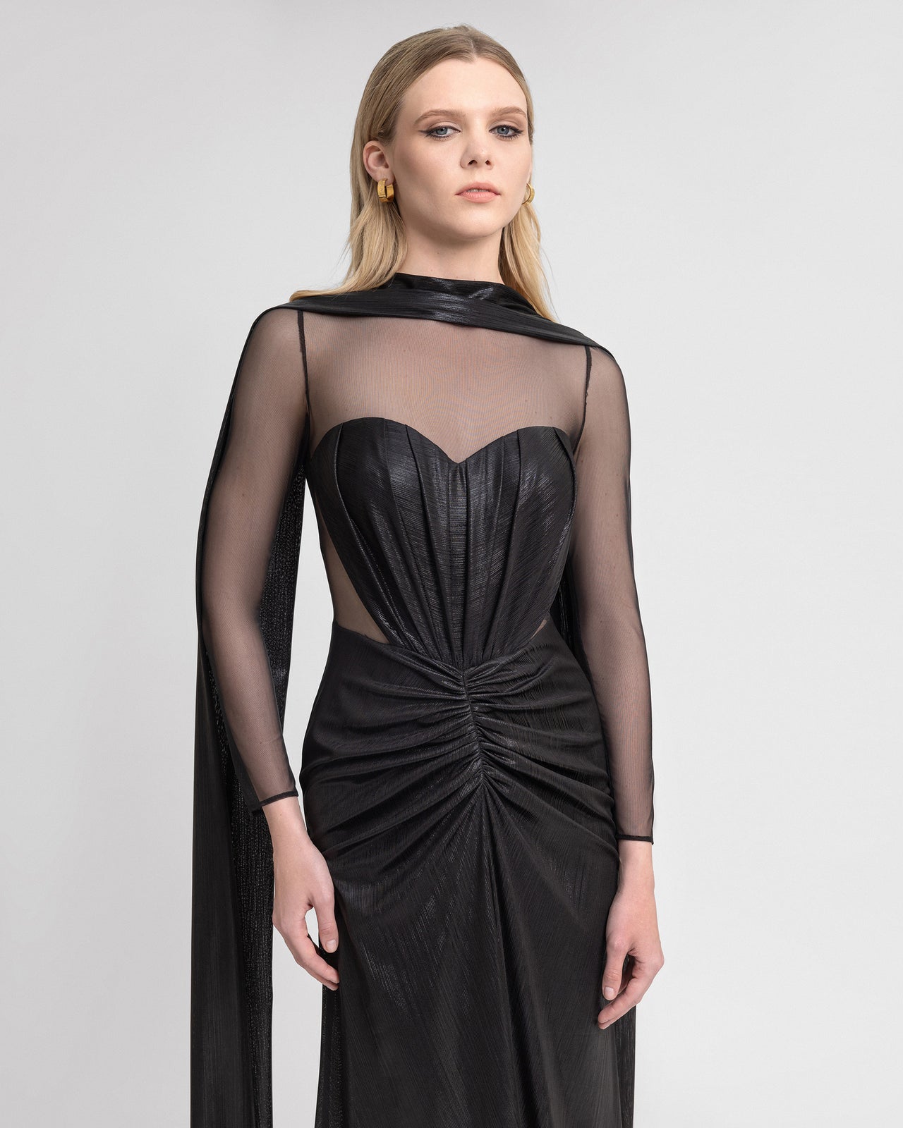 Video of a black lamé jersey gown with a heart-shaped neckline, sheer sleeves, gathered front, and dramatic cape overlay, showing the 120 cm hemline and flowing movement for bold, elegant eveningwear.