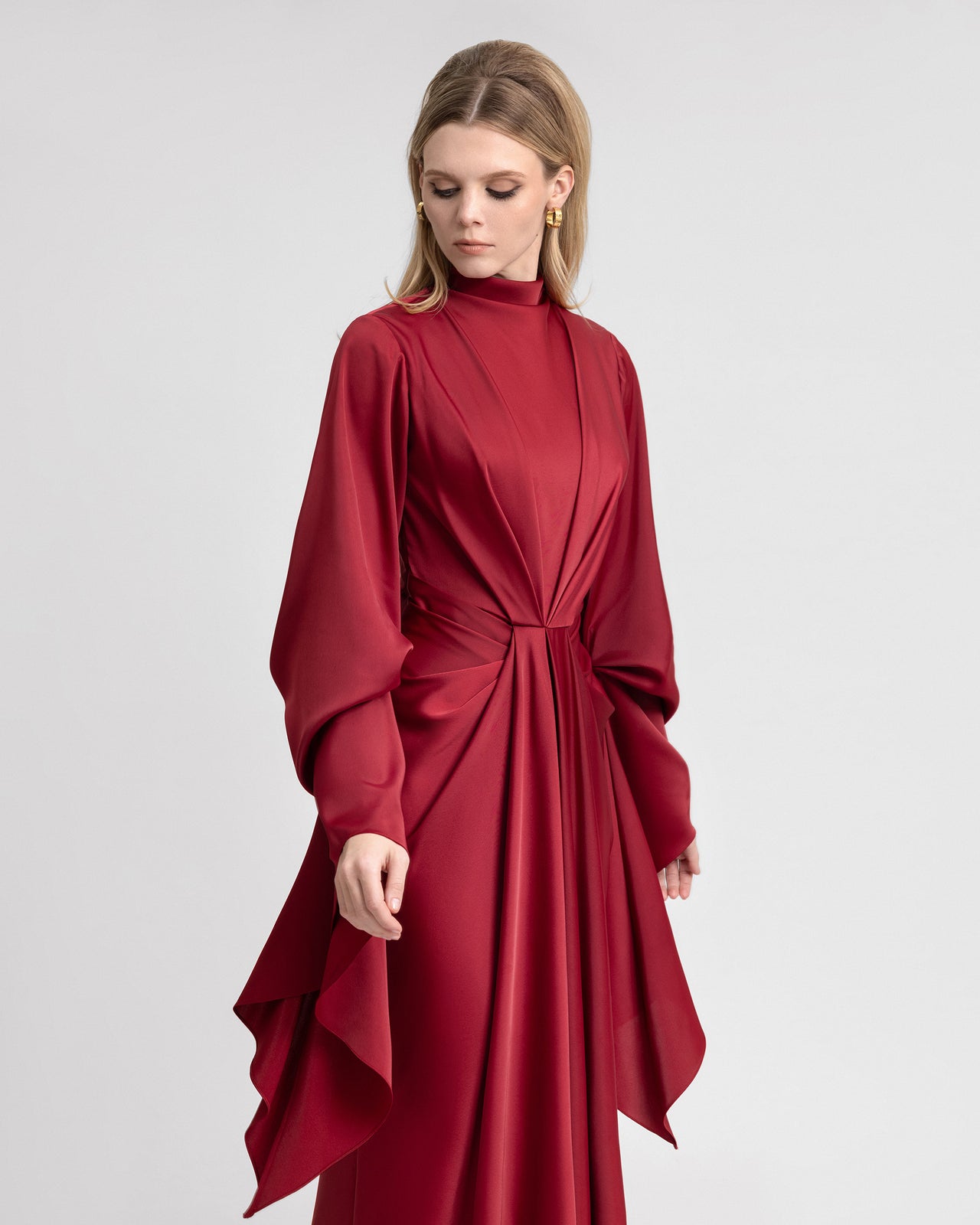 Video of a model showcasing a long satin dress with elegant waistline draping and dramatic long ruffled sleeves. The gown flows gracefully as the model moves, highlighting the luxurious texture and structured design of the satin fabric.
