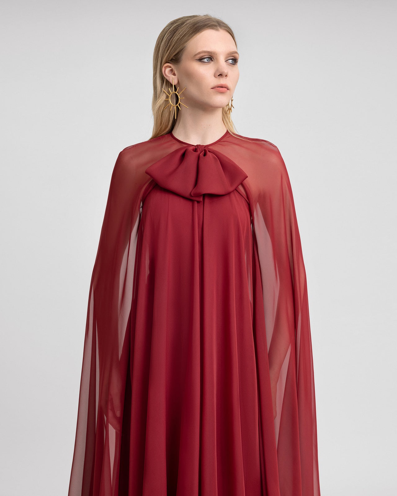 Video showcasing a flowy red chiffon dress with a large neckline bow, sheer cape sleeves, and open back, highlighting its elegant movement and design.