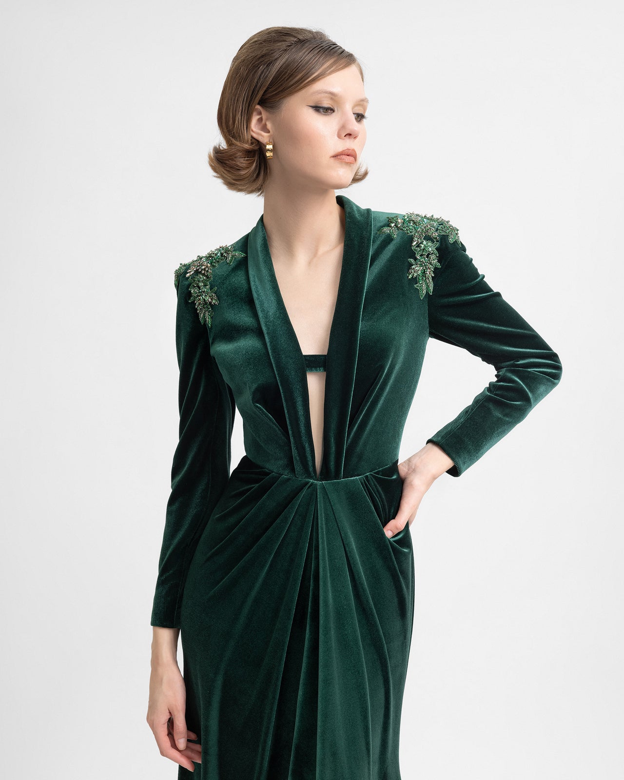 Video of a model wearing a green velvet gown with beaded shoulders, long sleeves, and a plunging chest cut-out, showing the dress’s structured details, back buttons, and elegant drape in motion.