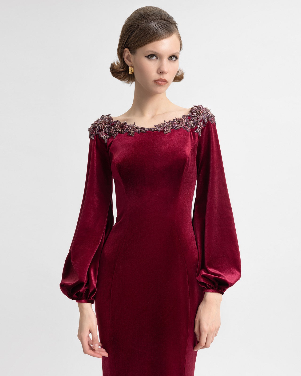 Video showcasing a model wearing a floor-length burgundy velvet gown with a beaded neckline, puffed sleeves, and an open back. The video highlights the dress's fit, flow, and intricate detailing