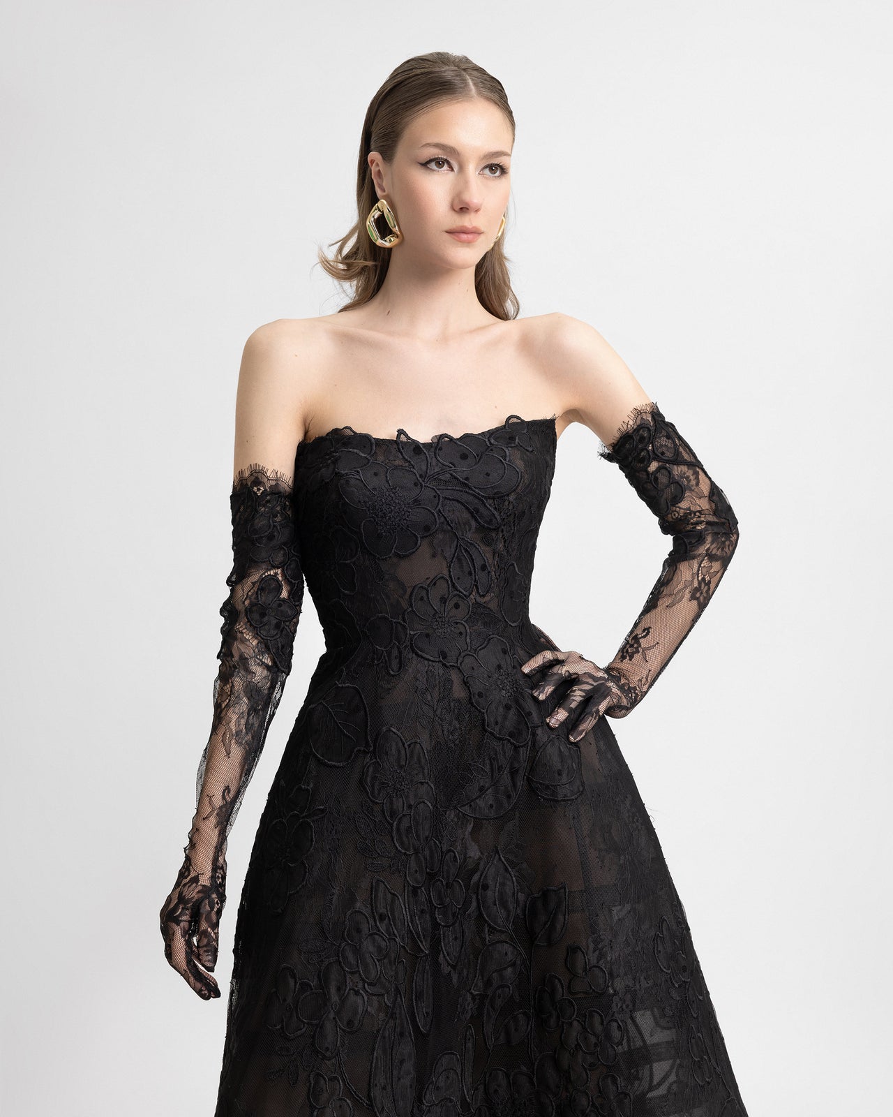 Video of a strapless black embroidered lace gown featuring a full cage skirt, styled with matching detachable lace gloves. The look emphasizes romantic drama with intricate floral lace, sheer detailing, and coordinated accessories.