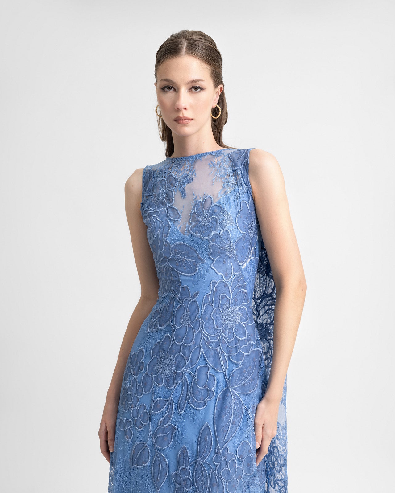 Video of a model wearing a sleeveless blue embroidered lace gown with a sheer neckline, dropped back, and flowing cape, highlighting the delicate floral details and elegant movement of the dress.
