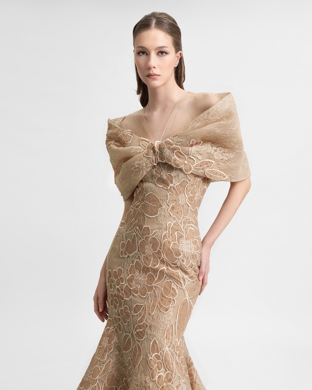 A model walks in a beige off-the-shoulder mermaid gown with floral lace embroidery and a dramatic draped bolero. The video highlights the gown’s fitted silhouette, flared hem, and textured lace details in motion.