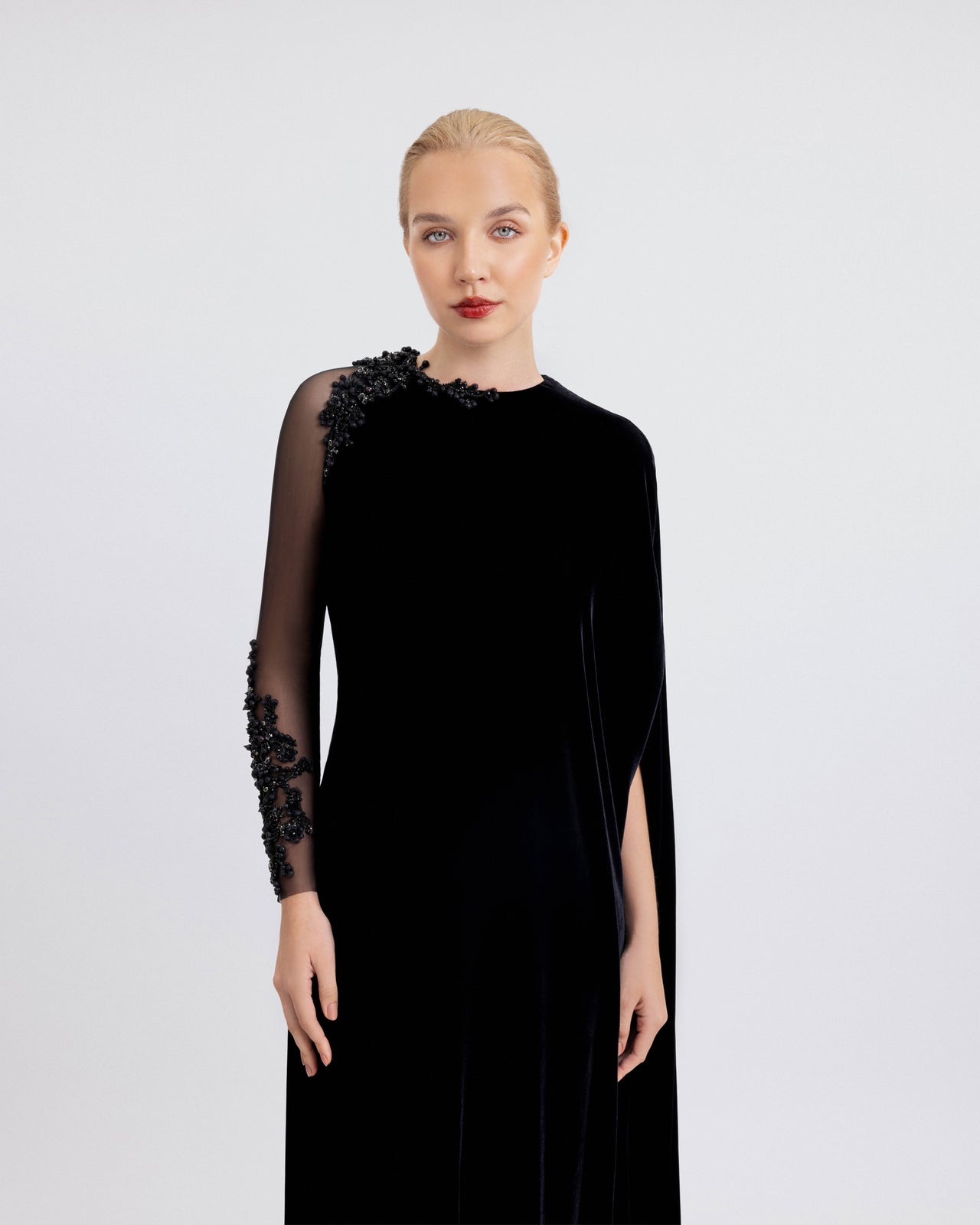 Video of a floor-length black velvet dress with a sheer beaded sleeve and a draped panel, shown in motion to highlight its elegant flow and details.