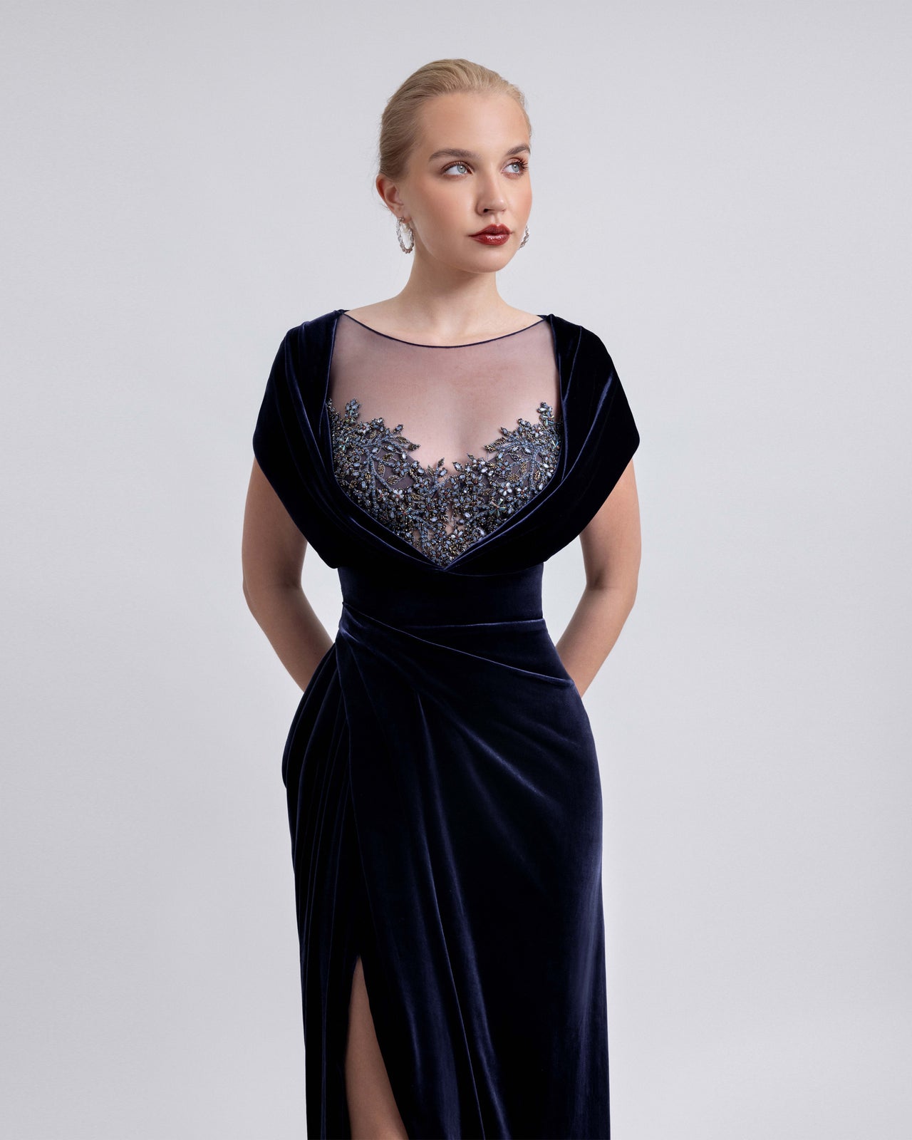 Video showcasing a navy velvet floor-length dress with a sheer beaded neckline and side slit. The clip highlights the front and back views, the fluid draping, and the intricate beading details in motion.