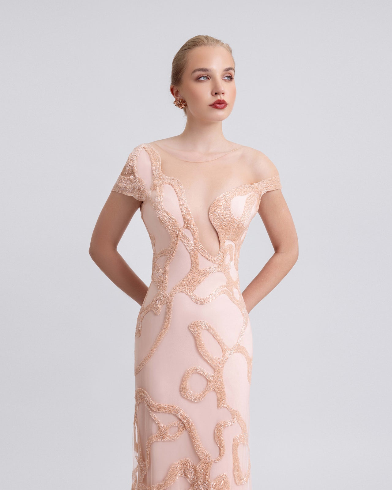 Video of a woman modeling a blush pink beaded gown with an asymmetrical neckline, sheer tulle overlay, and swirling embellishments, highlighting the plunging neckline and elegant movement of the 120cm floor-length design.