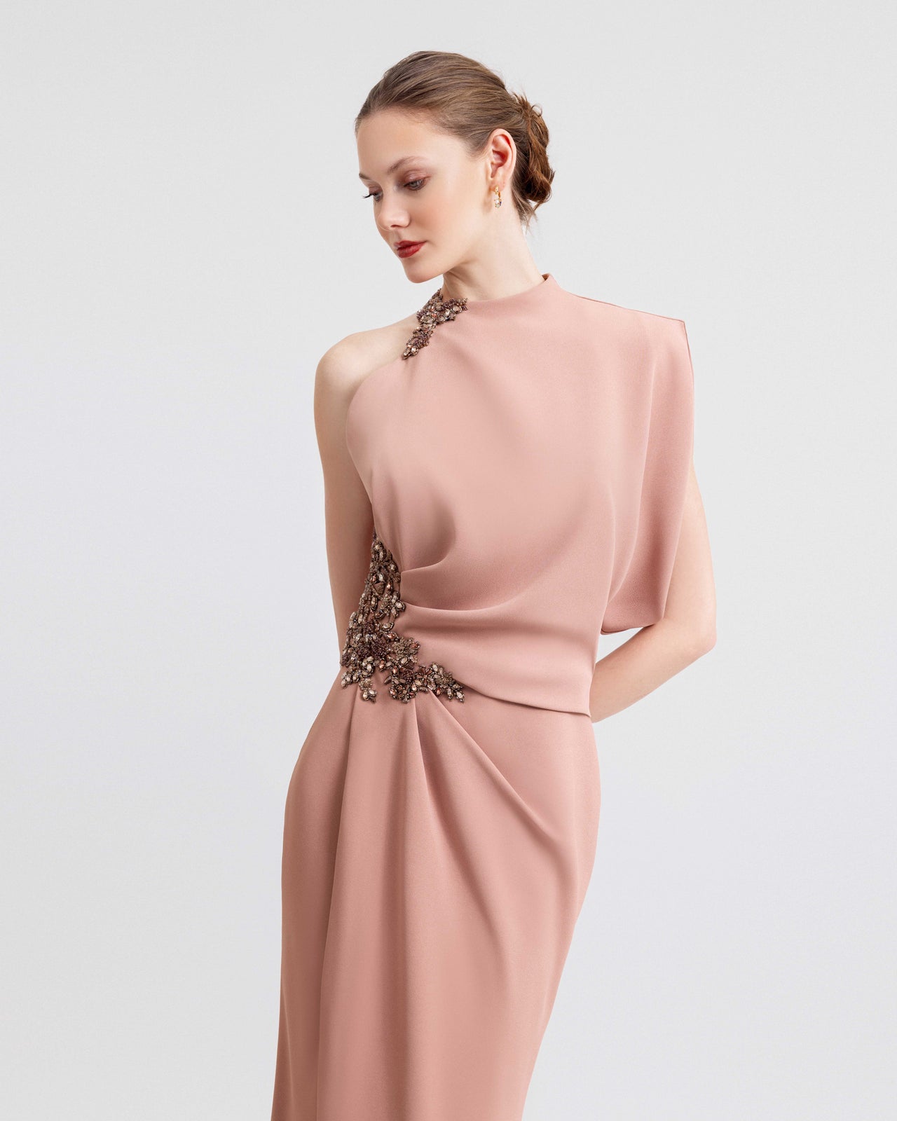  Video of a woman modeling a blush pink crepe gown with an asymmetrical neckline, side slit, and intricate beading at the collar and waist, highlighting the dress’s draped elegance and fluid movement.