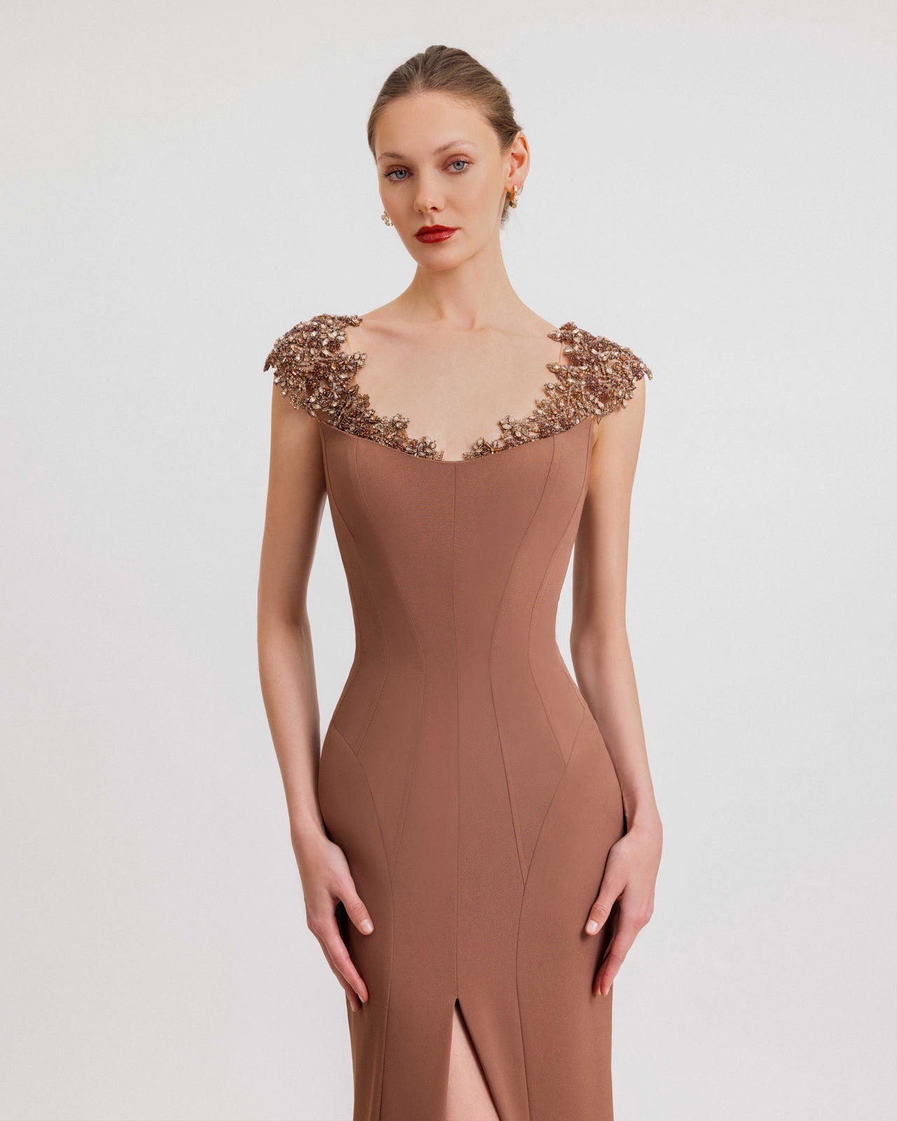 Video of a woman modeling a brown crepe evening gown with beaded tulle shoulders, a fitted silhouette, and a front slit, highlighting the dress’s elegant movement and detailed embellishment.