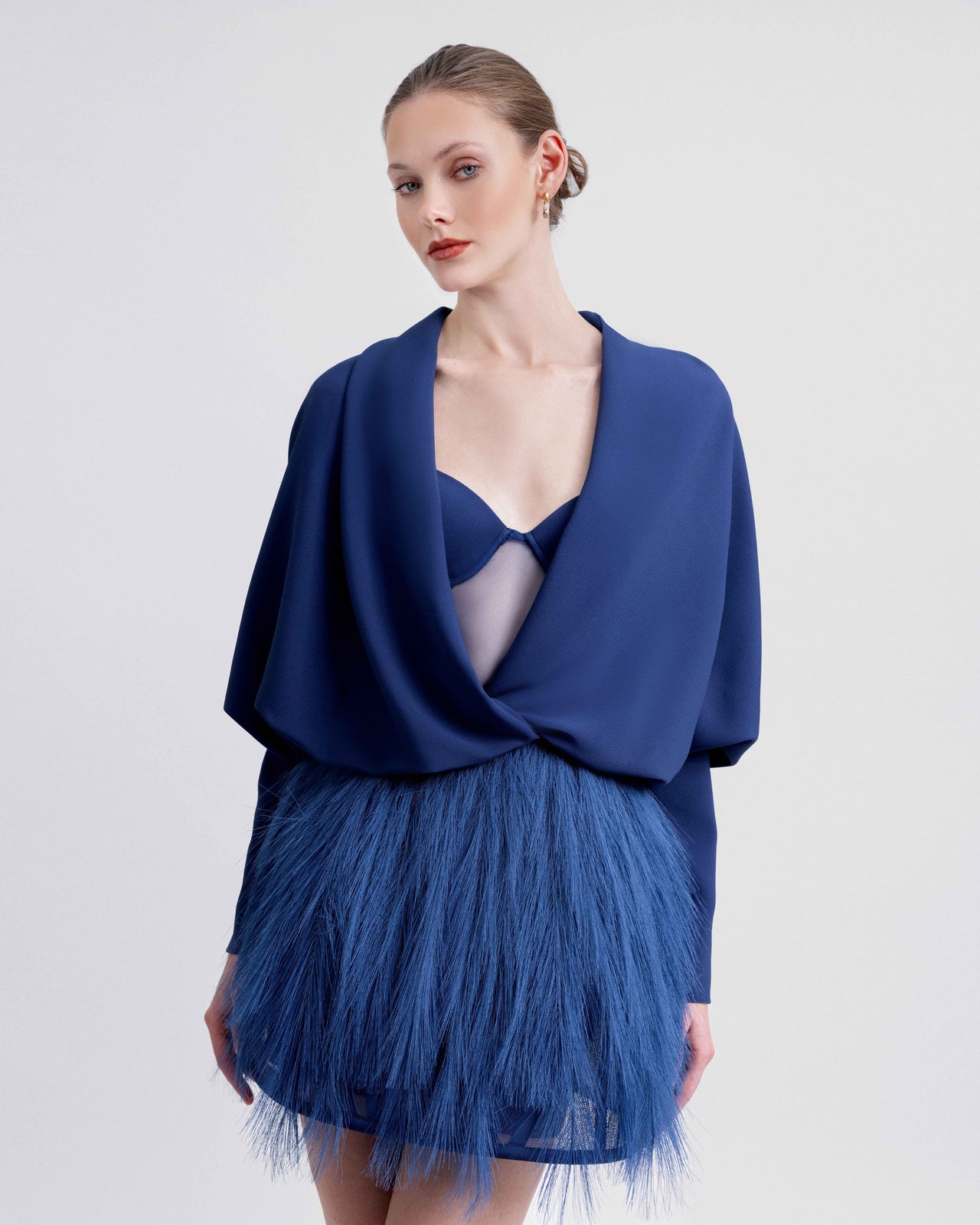 Video showcasing a short blue feathered dress styled with a plunging neckline draped crepe bolero. The video highlights the playful feather texture, elegant draping, and the overall movement of the outfit from various angles.