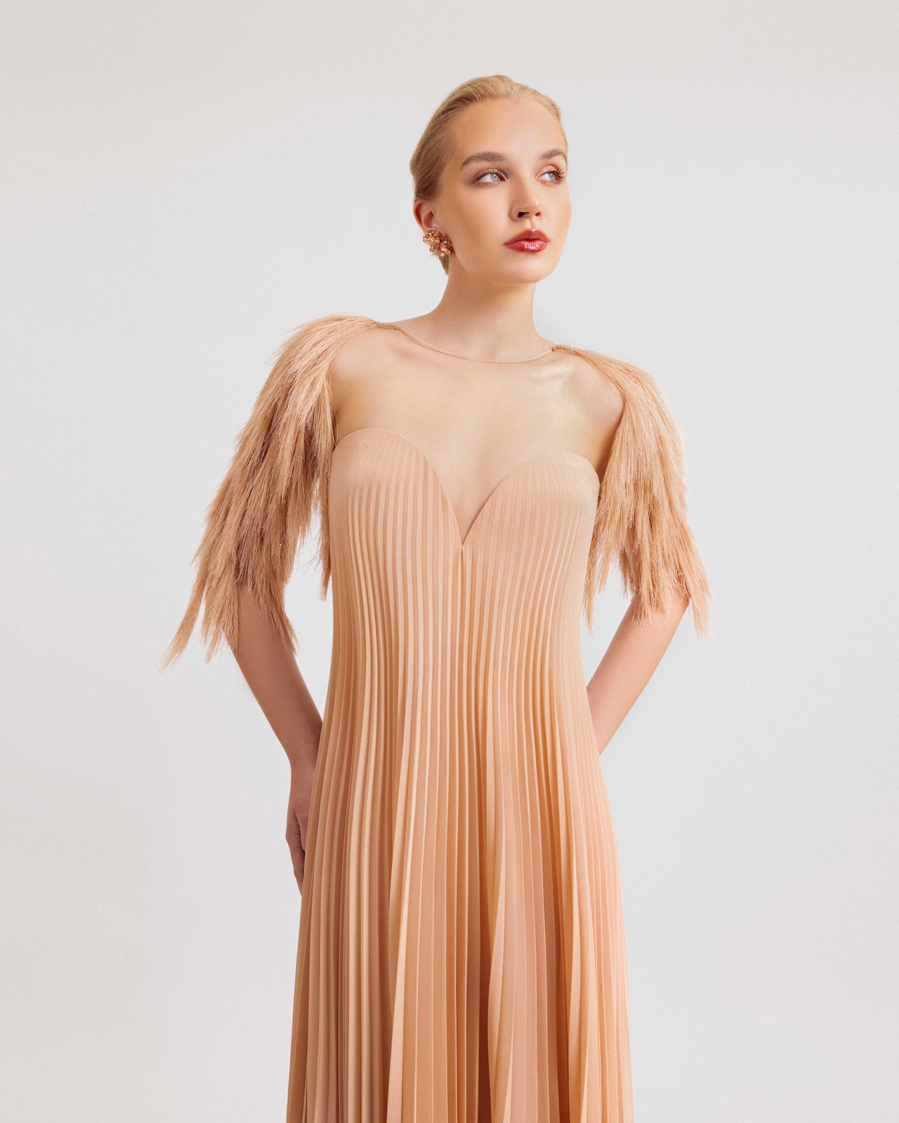 Video of a woman modeling a peach crepe georgette gown with feathered sleeves, a pleated skirt, heart neckline, and detachable belt, capturing the elegant flow and textural details in motion.