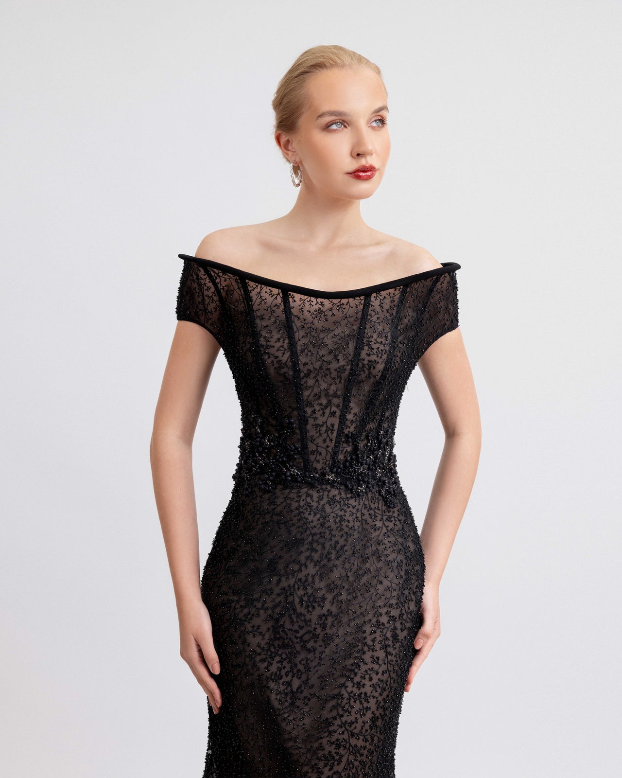Video of an off-the-shoulders black beaded gown featuring a sheer structured corset and detailed beadwork on the waistline, with the model walking and turning to showcase the dress’s fitted silhouette and flowing train.