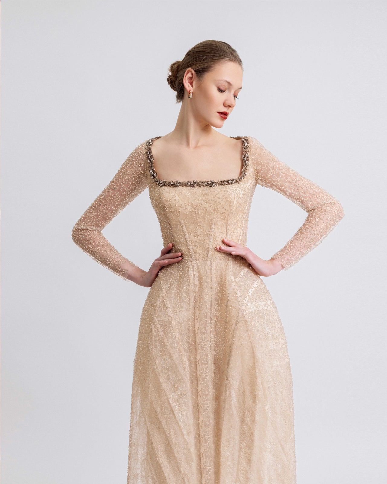 Video of a woman modeling a gold beaded gown with a square neckline, sheer embellished sleeves, and a structured underskirt, showcasing the gown’s detailed beadwork and graceful movement.