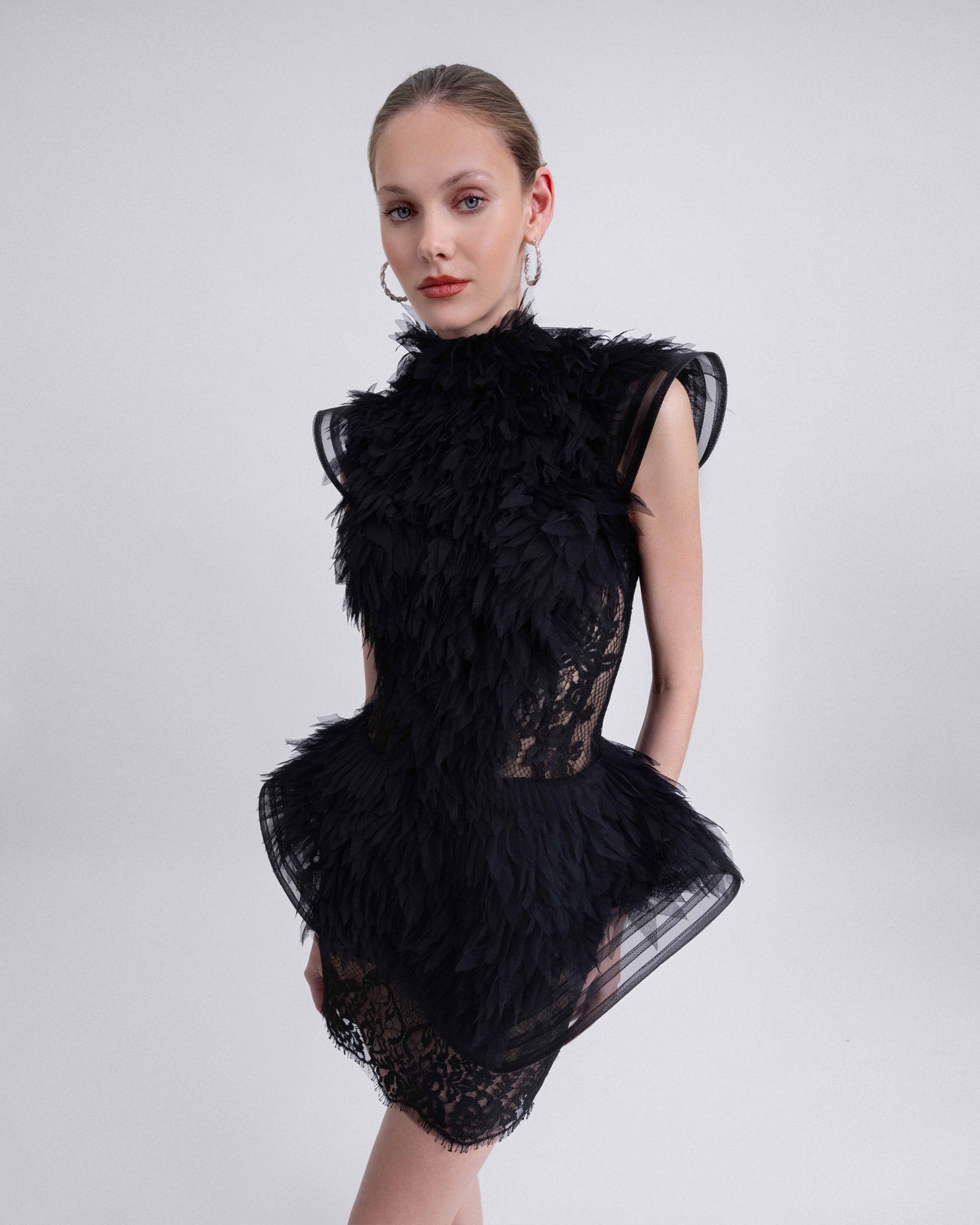  Video of a black mini dress with a high neckline, structured shoulders, and dramatic feathered embellishments. The dress features a sheer lace base with voluminous fringe and a peplum silhouette at the hips.