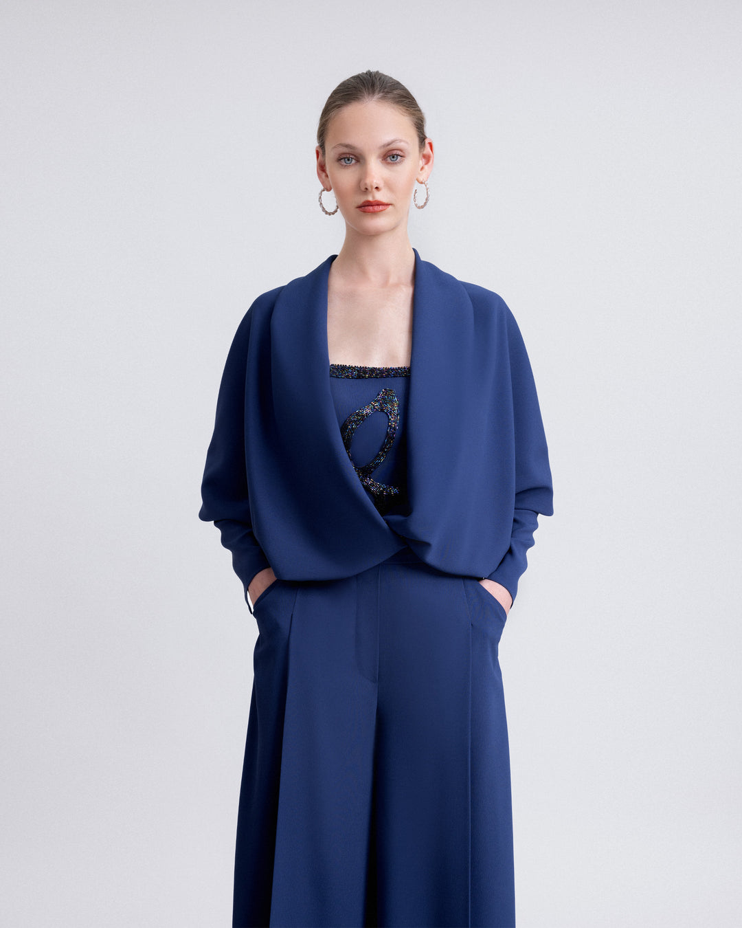 Video showcasing a navy ensemble with a strapless beaded top, straight-cut crepe pants, and a matching draped bolero with a plunging neckline. The video highlights the elegant movement, detailed beadwork, and sophisticated silhouette from multiple angles.