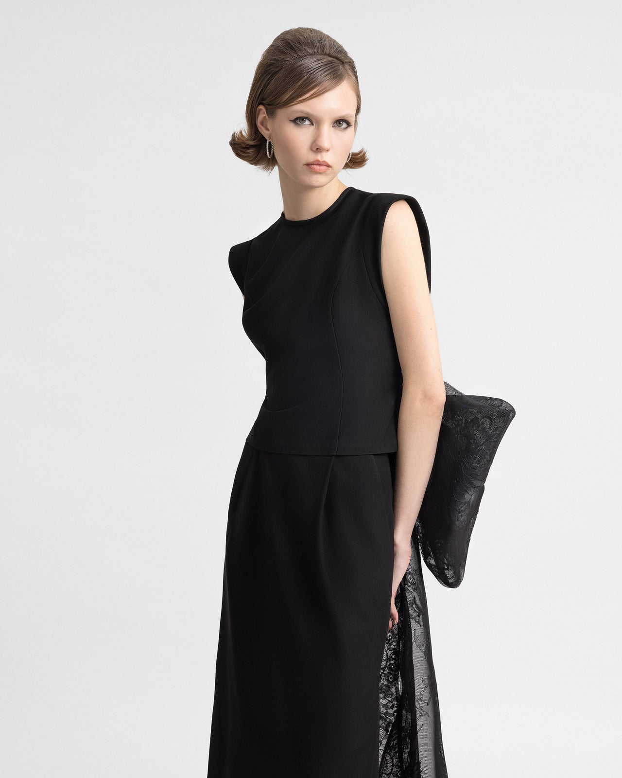 Video showcasing a black crepe top with a sheer lace back and a voluminous textured lace bow, paired with a long skirt featuring high side slits and a flowing lace train. The video captures the contrast between structured tailoring and soft, romantic lace details in motion.