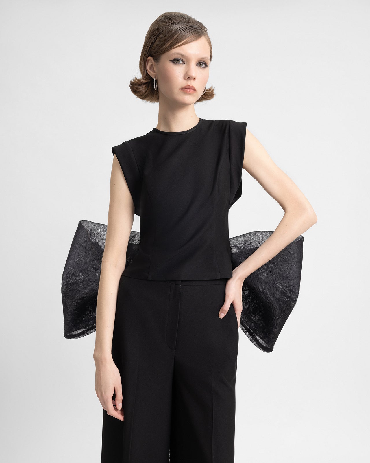 ideo showcasing a black crepe outfit with a sheer lace back, structured sleeveless top, and wide-leg pants, finished with an oversized sculptural lace bow and flowing lace train. The set highlights a blend of sharp tailoring and feminine lace details in motion.