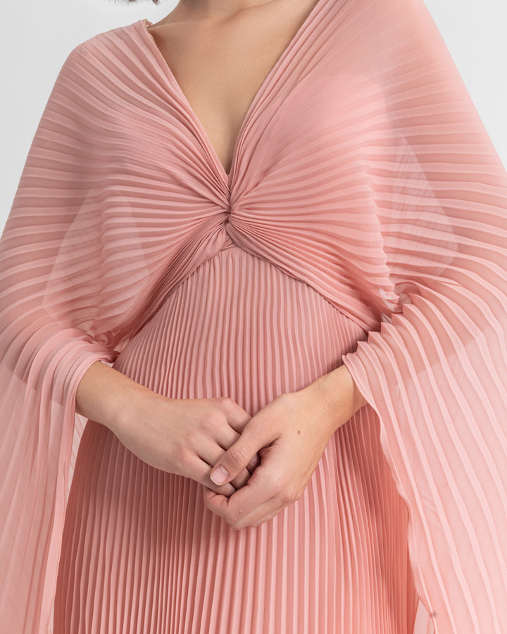 A close-up of a V-neckline fully pleated flared chiffon dress in pink with draping details.